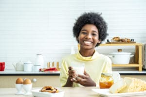 Happy cute African-American boy drinking milk and eating bread with egg.
