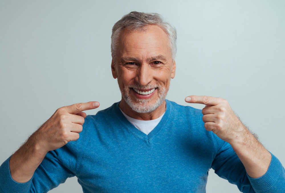 Man smiling and pointing to his teeth with his new dental crown in McLean, VA