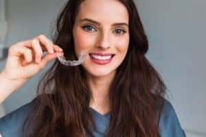 Woman smiling and holding up her Invisalign tray in McLean, VA