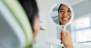 Woman looking in the mirror at the dentist smiling after getting a dental implant in McLean, VA.